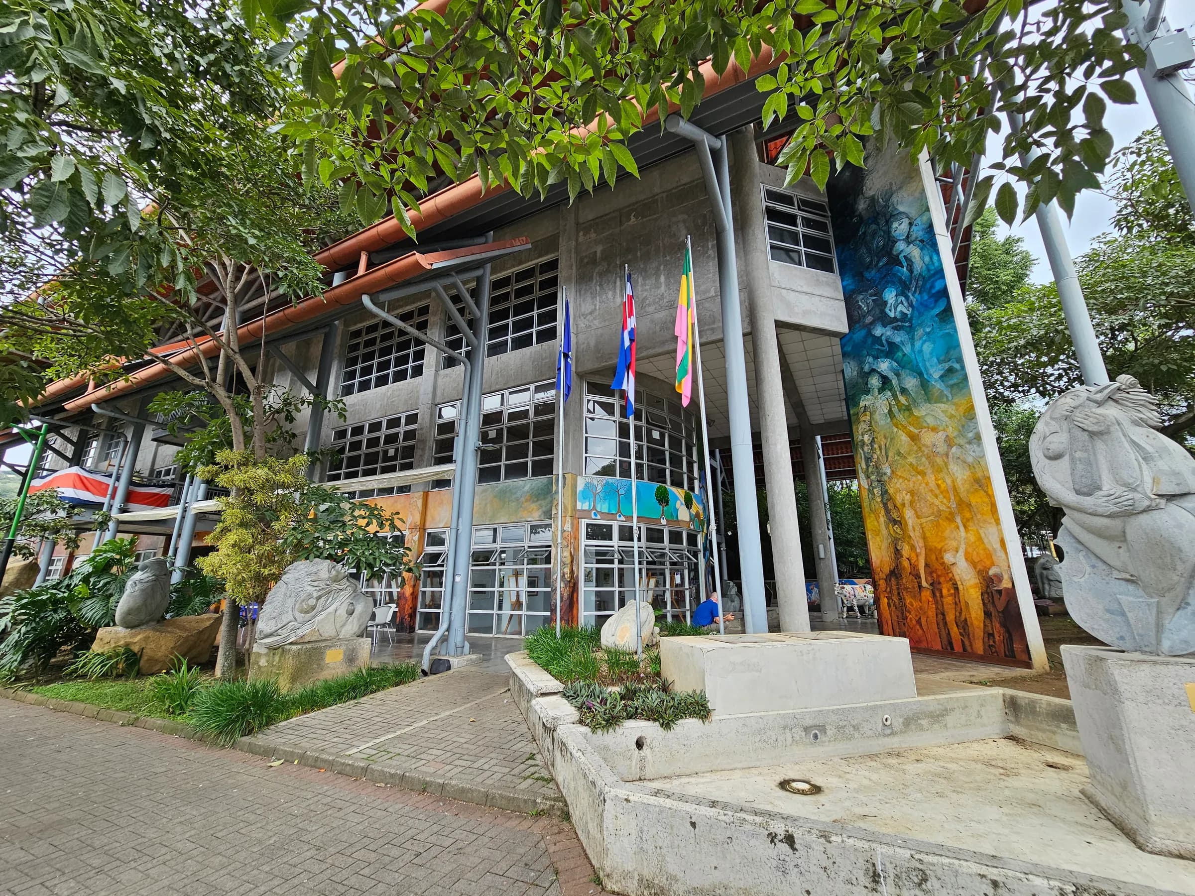 Fachada del edificio de la EMAI con su gran mural en tonos azules y ocres, esculturas en piedra y banderas